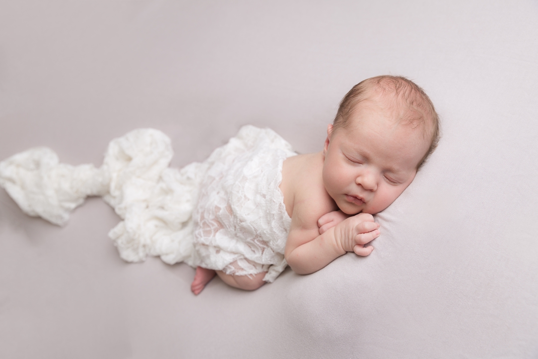 Newborn studio photographer hayley morris sleeping Baby posed on a posing beanbag with grey backdrop, white wrap and headband 
